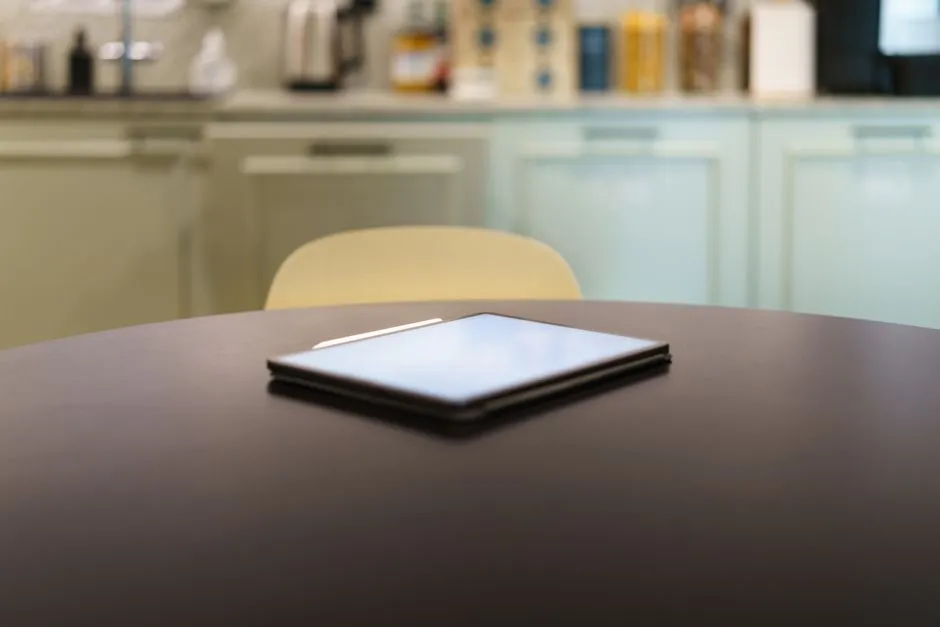 Tablet on a kitchen table next to a finished homework book, showing a spelling game with letter tiles