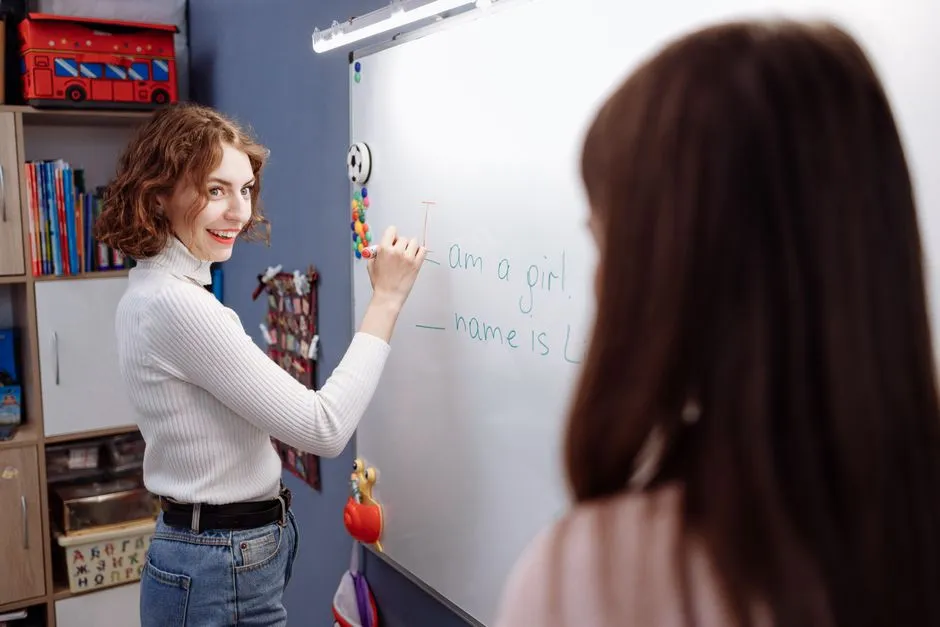 Teacher writing a class code on a whiteboard while students play a quiz on classroom tablets